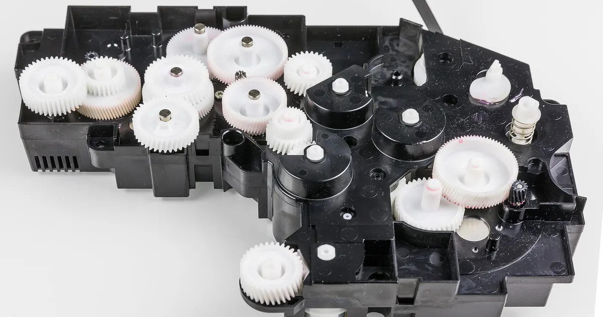 White plastic gears in a printer drive module, the kind of precision part where acetal vs PET is decided