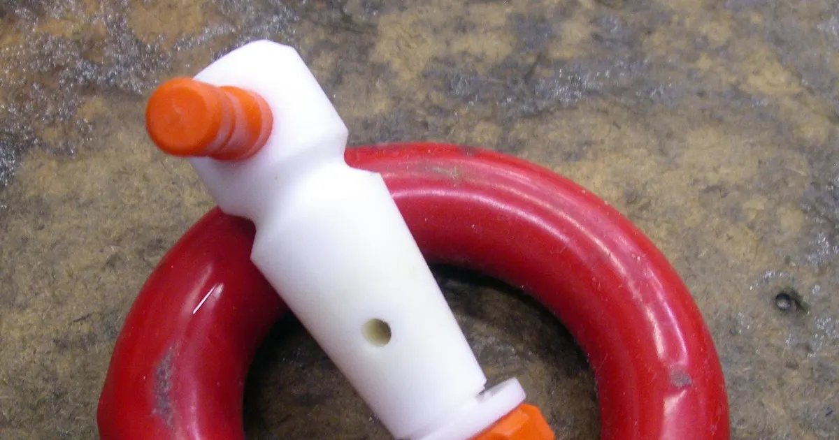 White PTFE stopcock plug with a retaining nut inside a red ring, a machined fluoropolymer part for comparing acetal vs PTFE