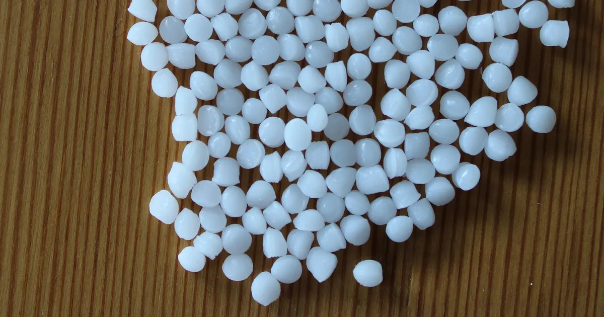 Natural white POM resin granules on a wooden table, the base material behind black vs natural Delrin stock
